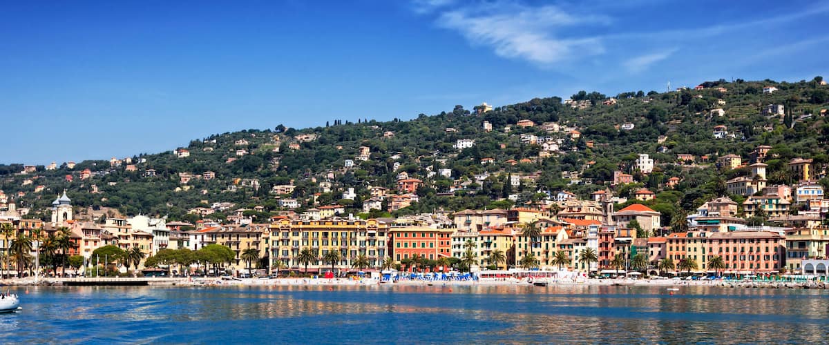 A coastal town with colorful buildings, a marina, and a hillside with scattered houses.