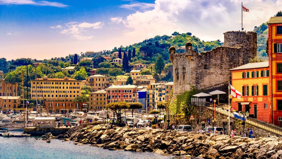 A coastal town with a historic castle, colorful buildings, and a marina.