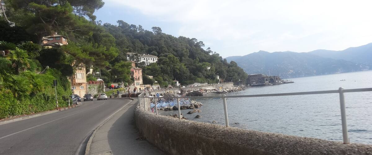 A coastal road with a stone wall, a bridge, and a body of water with boats.