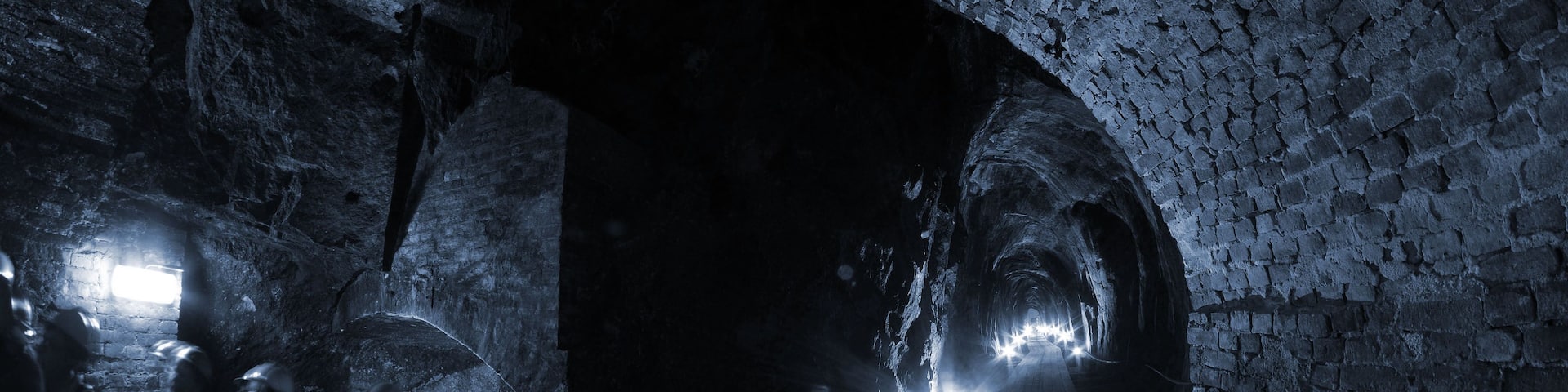 A dimly lit underground tunnel with brick walls and wooden planks on the floor.