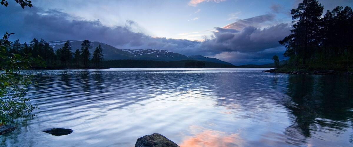 A calm lake with a mountain in the background and a cloudy sky.