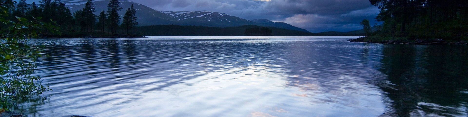 A calm lake with a mountain in the background and a cloudy sky.