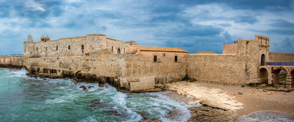 A coastal fortress with a stone wall and a tiled-roof building.