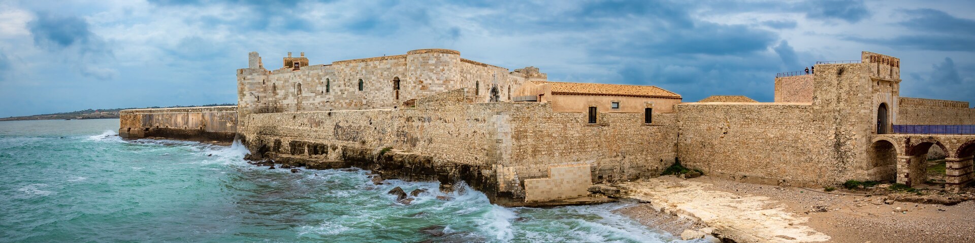 A coastal fortress with a stone wall and a tiled-roof building.