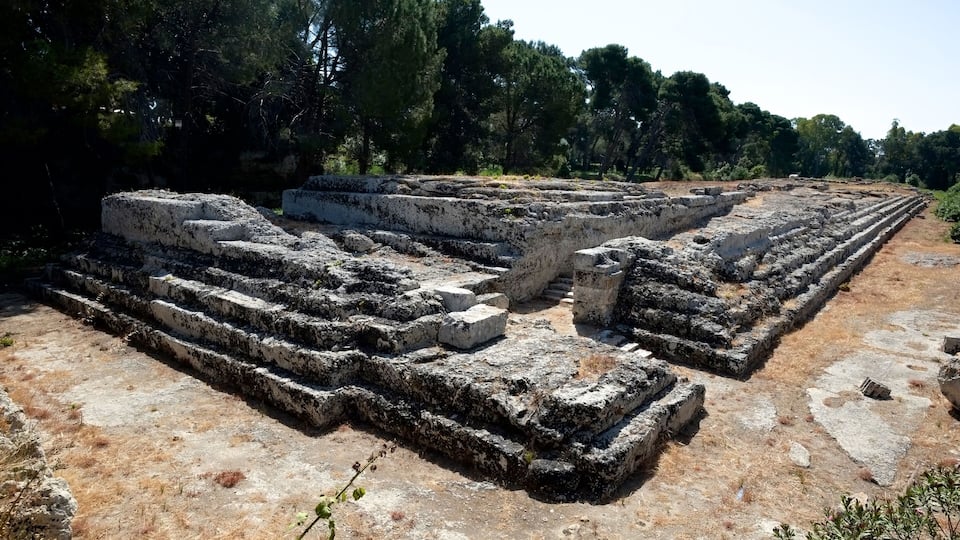 Ancient ruins with stone steps and walls, surrounded by trees.
