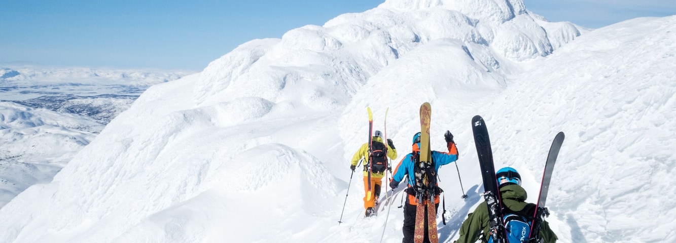 Un grupo de esquiadores subiendo una montaña nevada bajo un cielo despejado.