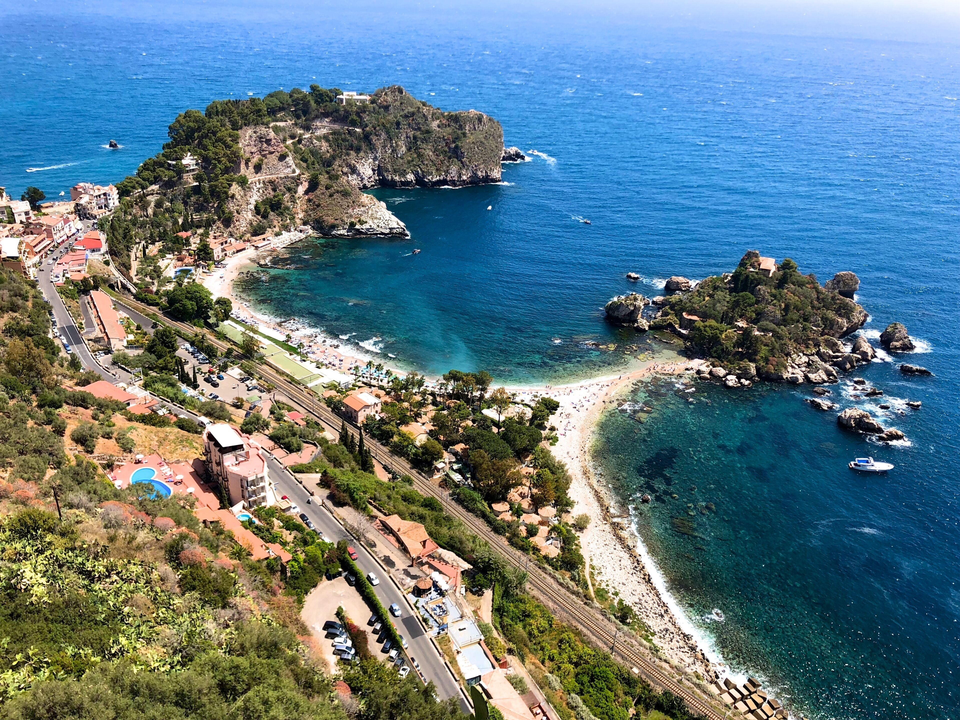 A coastal town with a beach, rocky outcrops, and a clear blue sea.