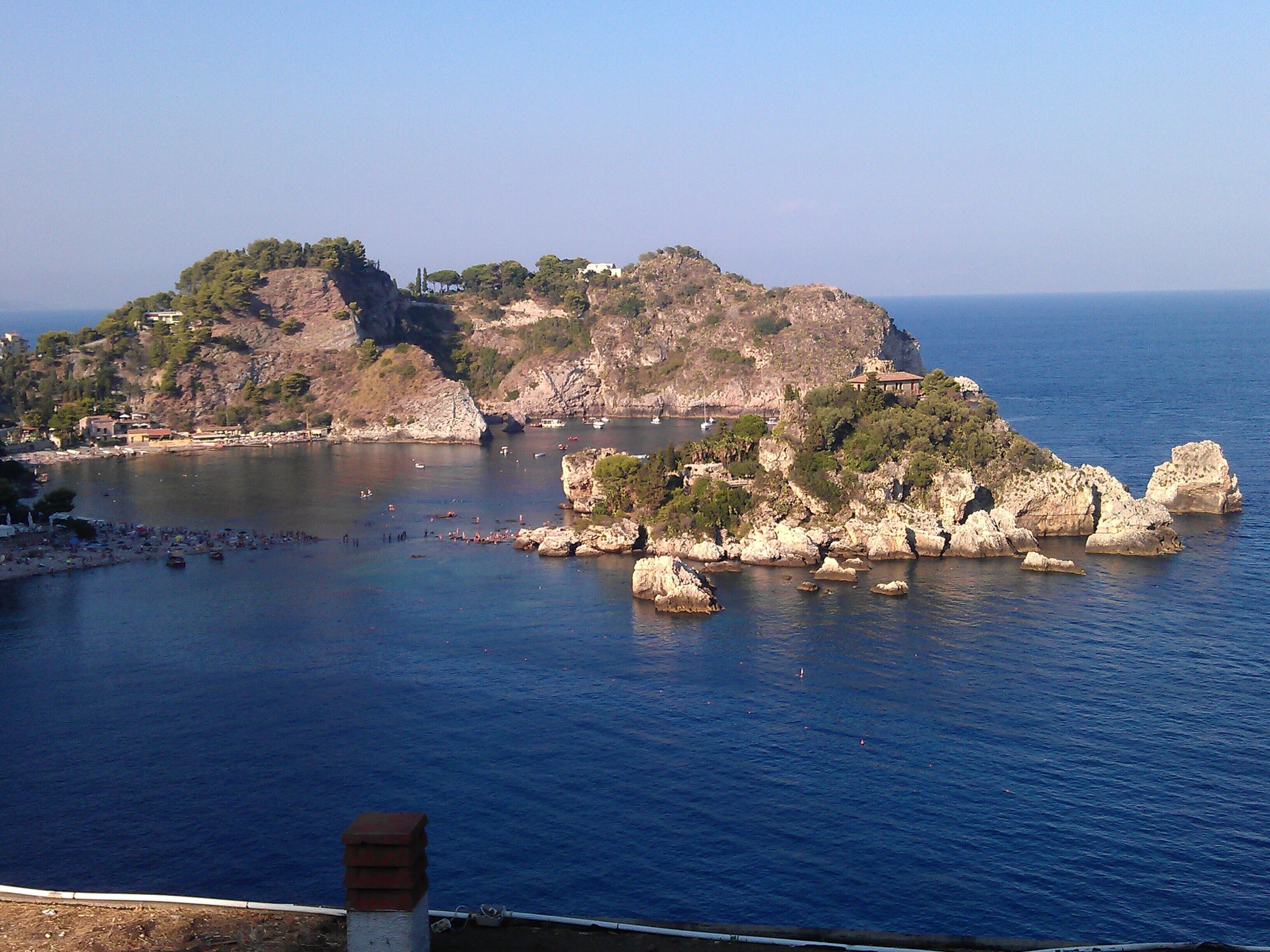 A coastal landscape with rocky formations, a small island with buildings, and calm sea.