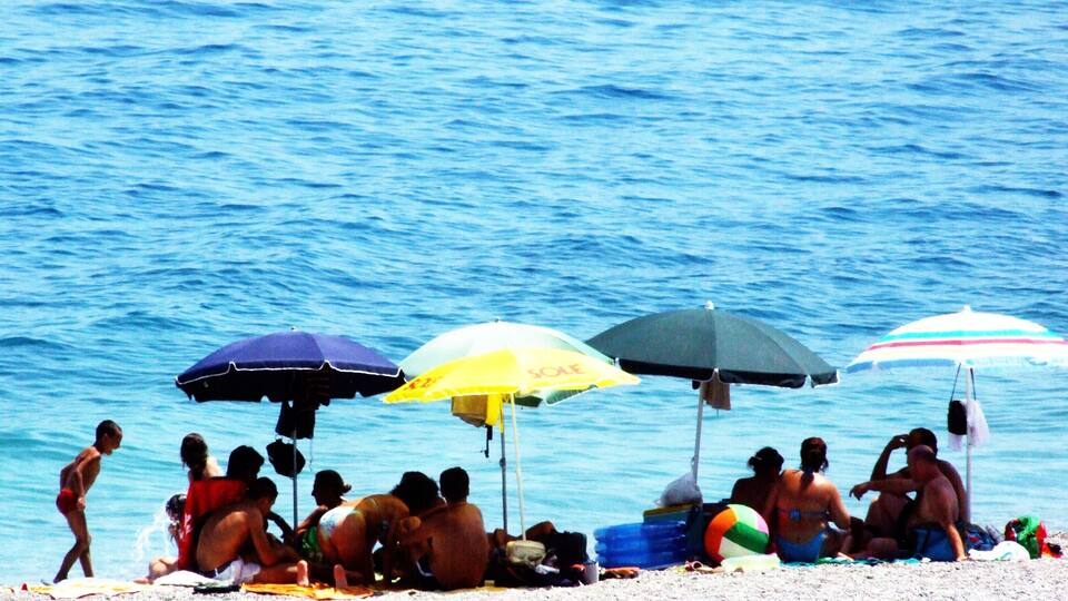 A beach with people relaxing under umbrellas and a volleyball on the sand.