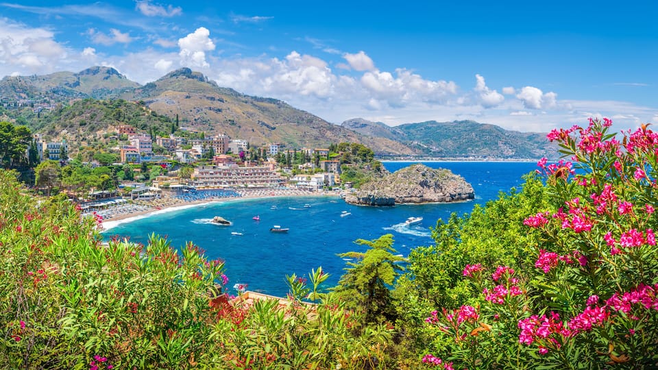 A coastal town with a beach, boats, and mountains in the background.