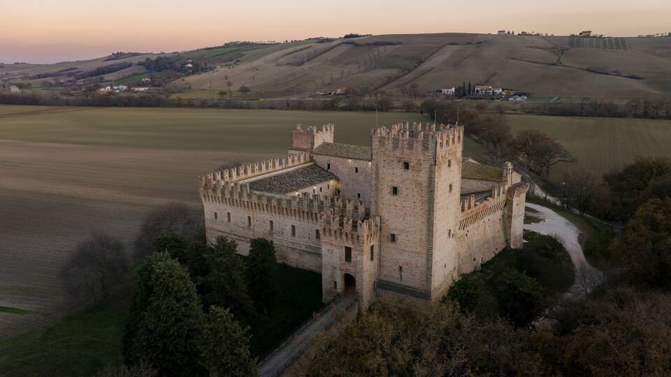 A medieval castle surrounded by fields and hills.