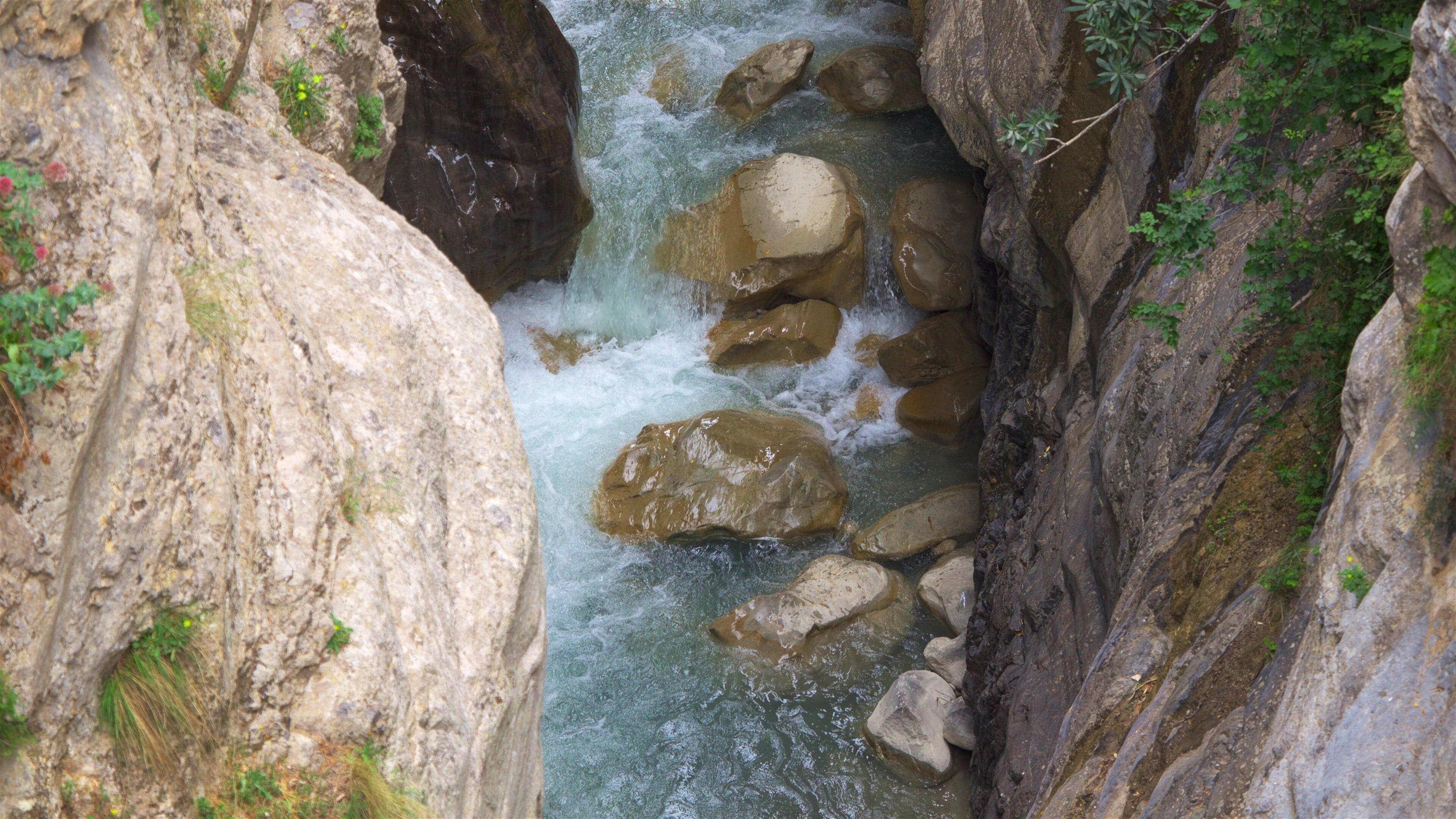 A narrow canyon with a fast-flowing river, large boulders, and rocky walls.