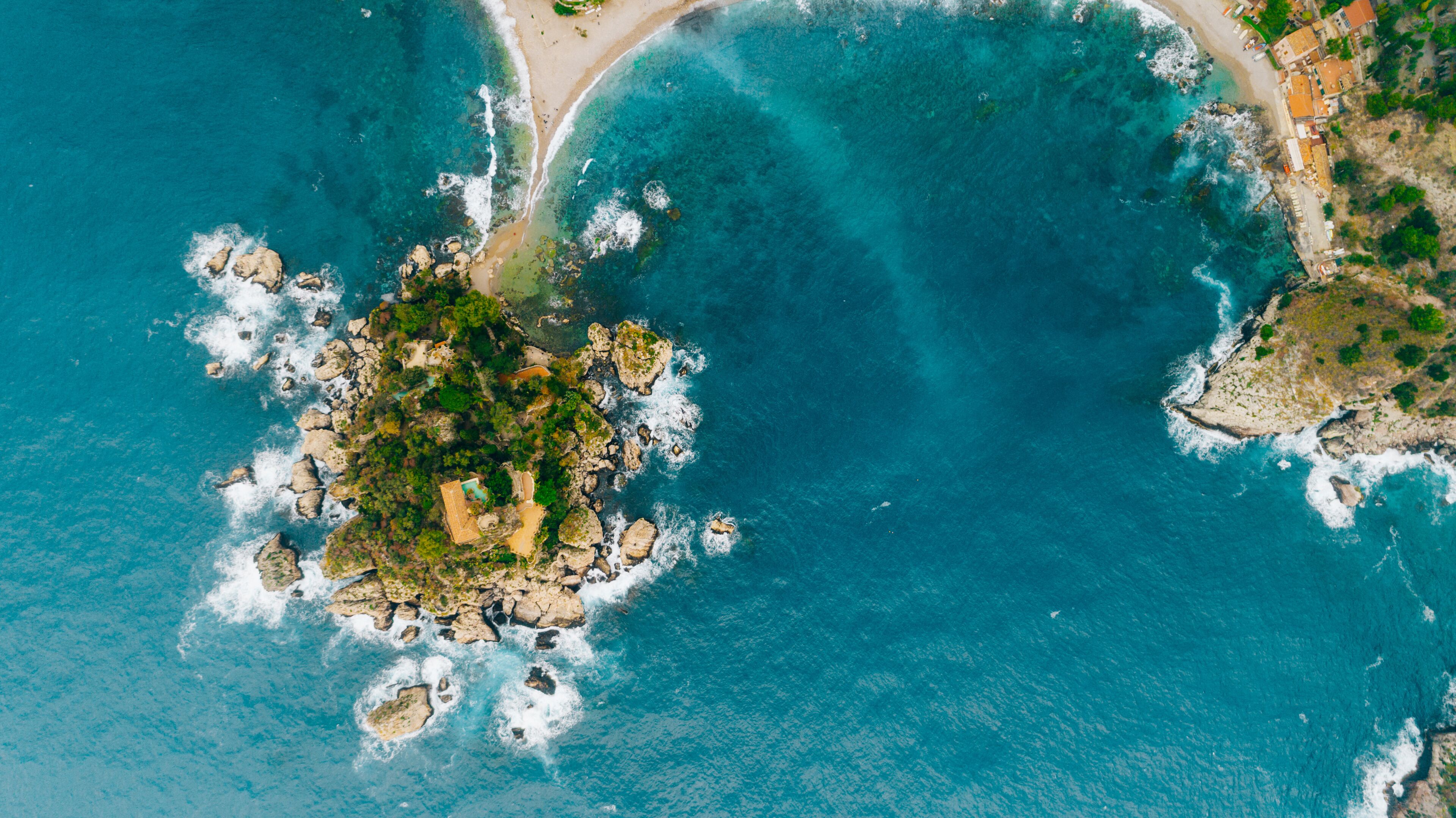 A coastal landscape with clear turquoise waters, rocky outcrops, and a small island with greenery.