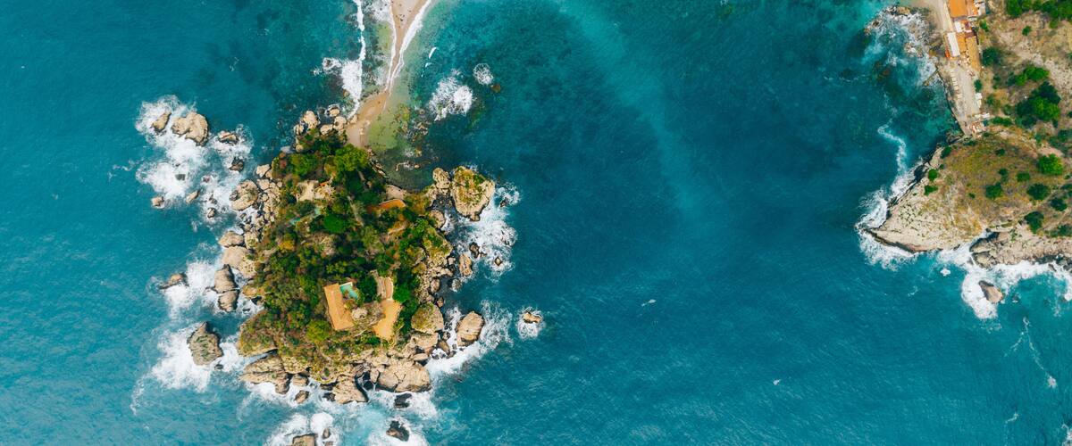 A coastal landscape with clear turquoise waters, rocky outcrops, and a small island with greenery.