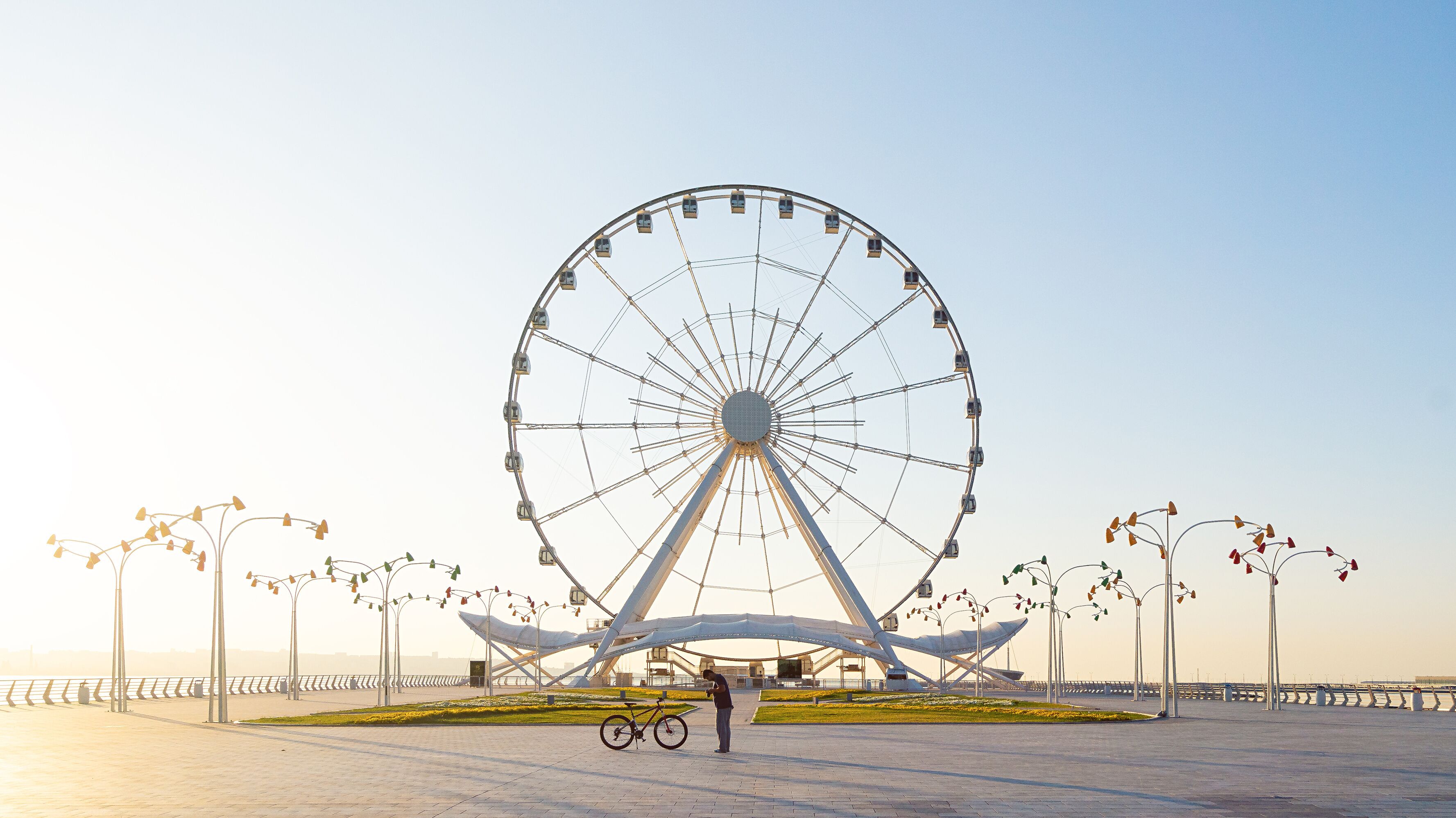 Uma grande roda gigante com gôndolas, uma bicicleta e uma pessoa parada por perto.
