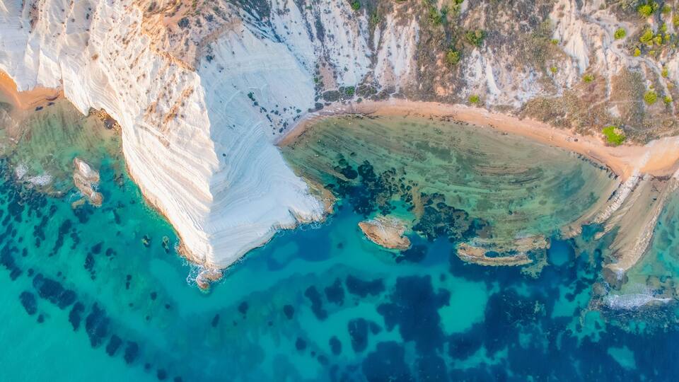 A coastal cliff with white rock formations and clear turquoise waters.
