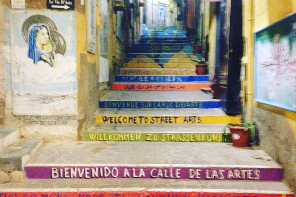 Un estrecho callejón con escalones coloridos que conducen a una puerta, decorada con varios letreros y grafitis.