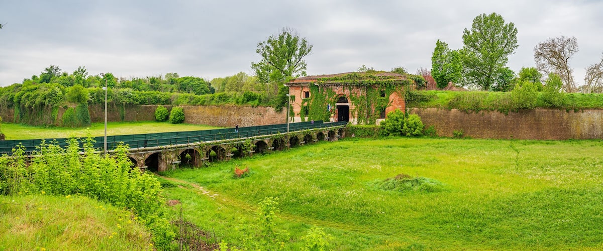 A green bridge over a moat, surrounded by lush greenery and brick walls.