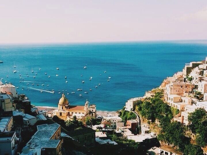 A coastal town with a prominent church dome, a densely packed hillside with buildings, and a marina with numerous boats.