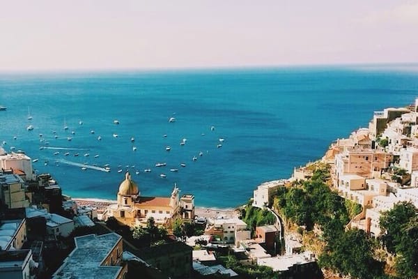A coastal town with a prominent church dome, a densely packed hillside with buildings, and a marina with numerous boats.
