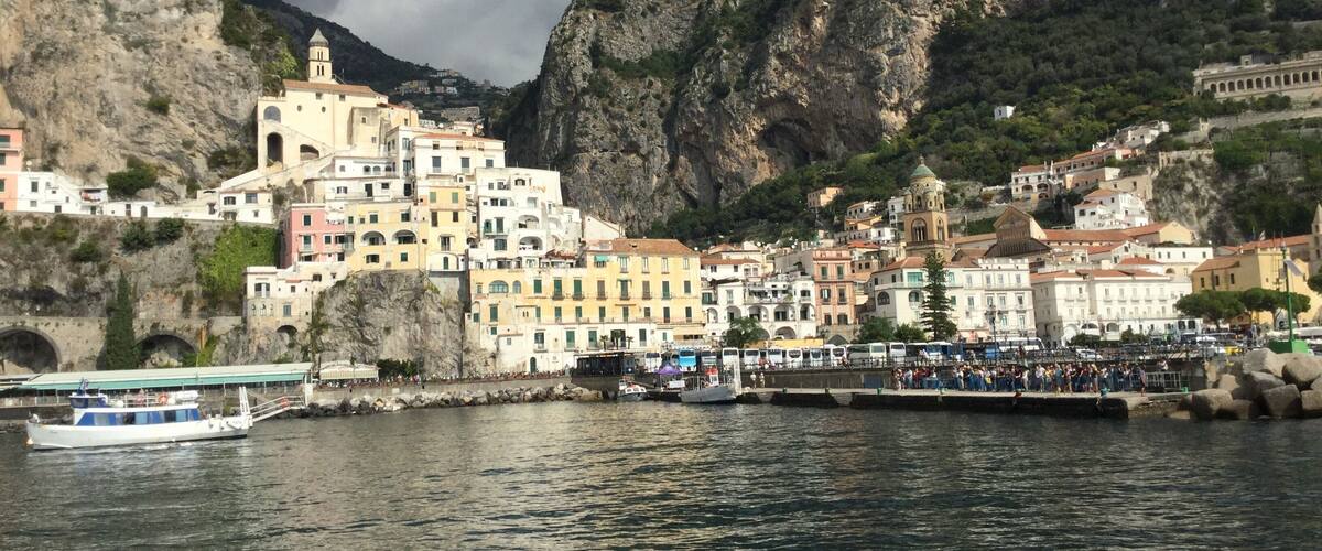 A coastal town with colorful buildings, a church, and a rocky mountain backdrop.