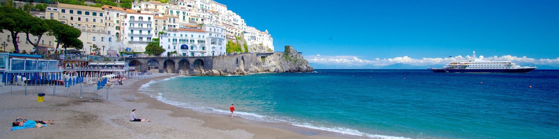 Un pueblo costero con edificios blancos, una playa y un crucero al fondo.