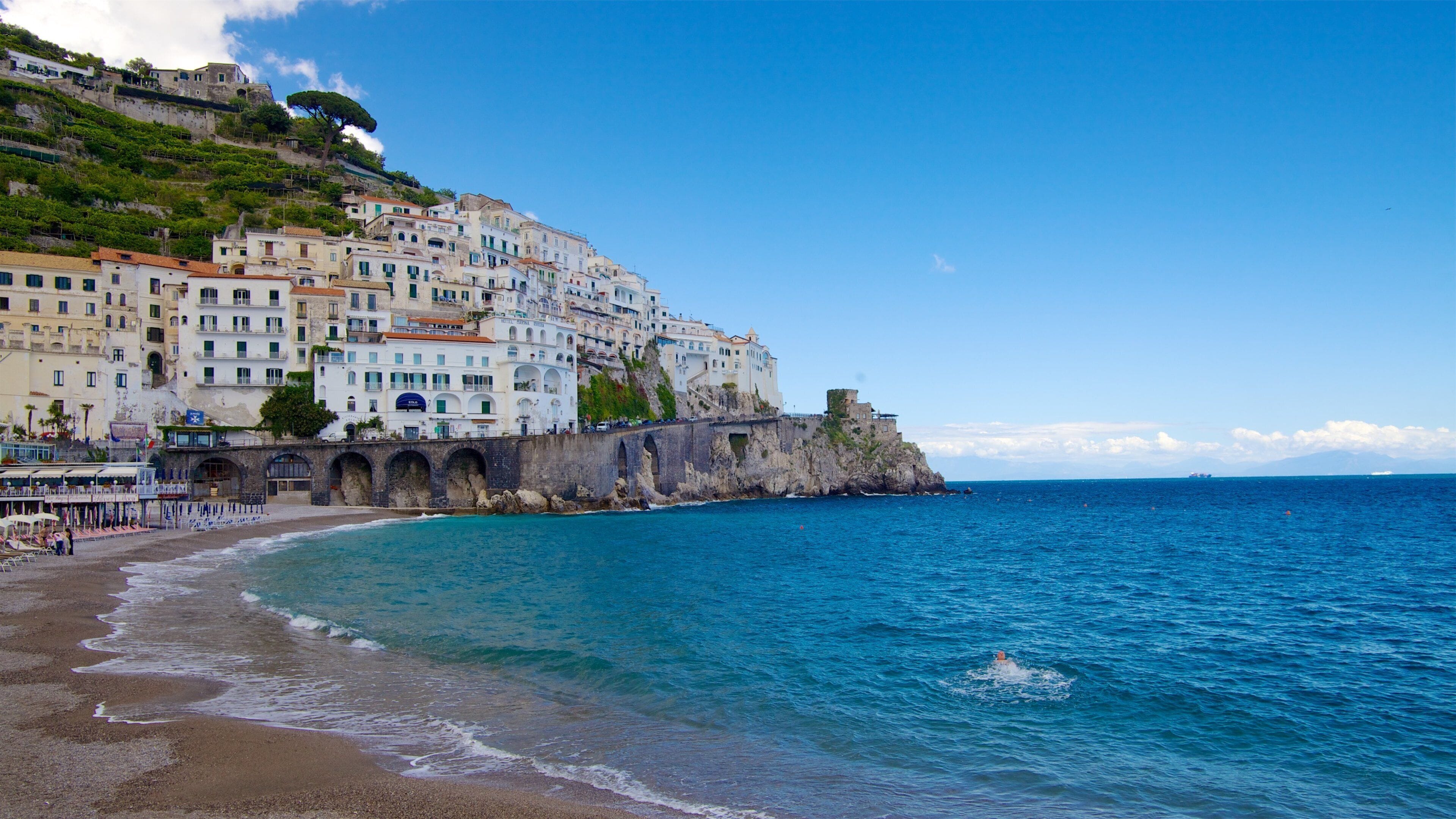 A coastal town with white buildings, a beach, and a rocky cliff.