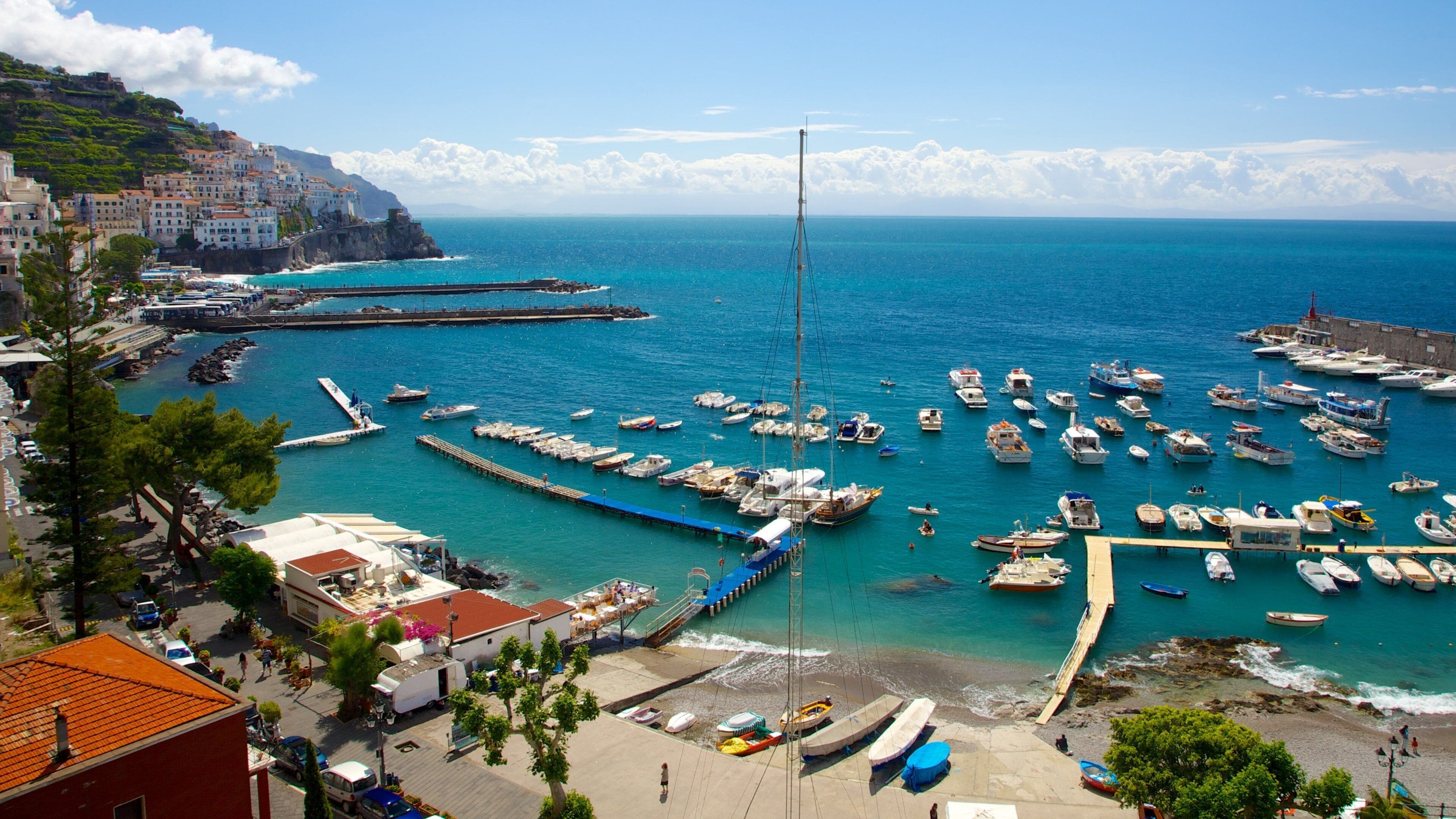 A coastal town with a marina filled with boats, a lighthouse, and buildings along the cliffside.