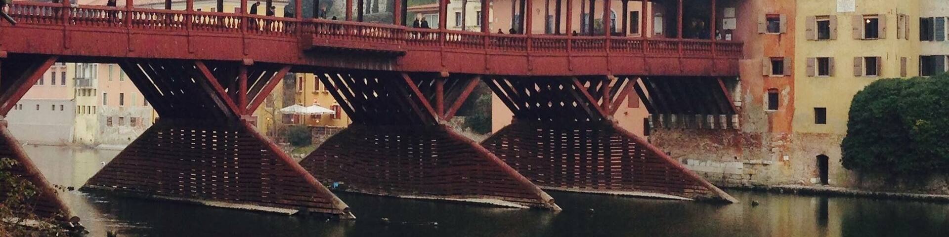 A red metal bridge over a river with buildings in the background.