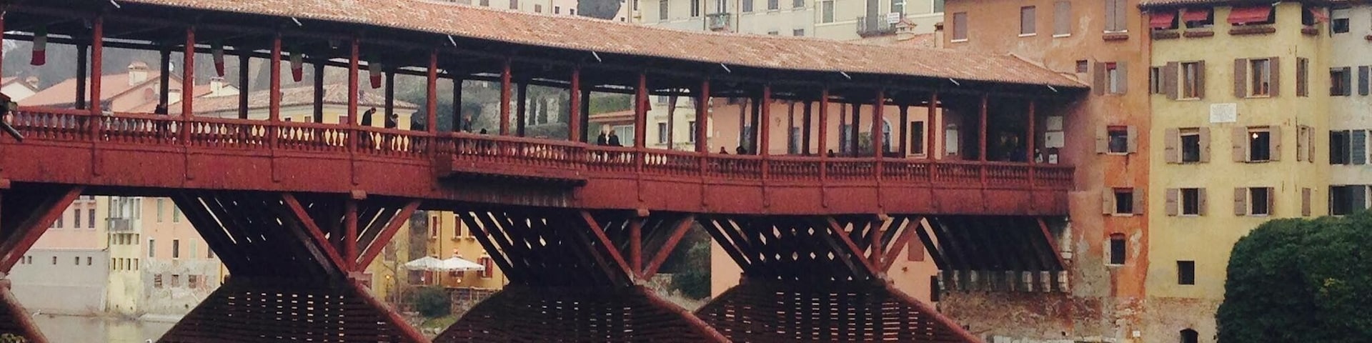Uma ponte de metal vermelha sobre um rio, com edifícios ao fundo.