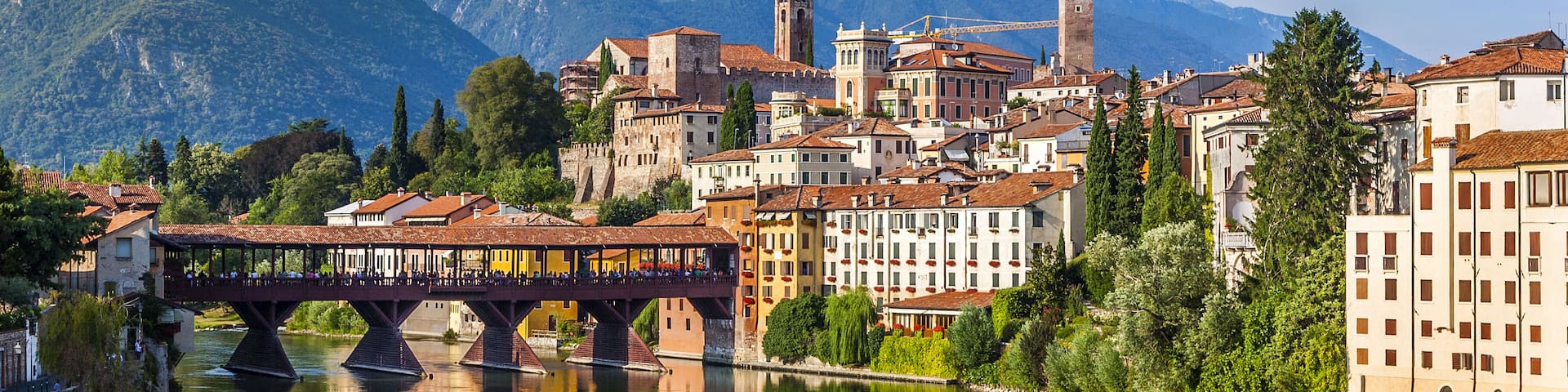 A river with a bridge, buildings, and mountains in the background.
