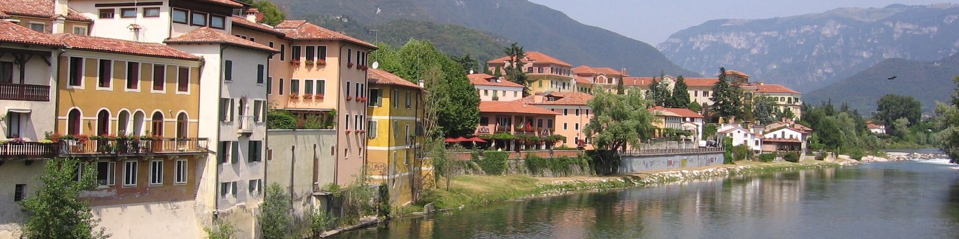 Un río con edificios a lo largo de sus orillas, una cadena montañosa al fondo y un cielo despejado.