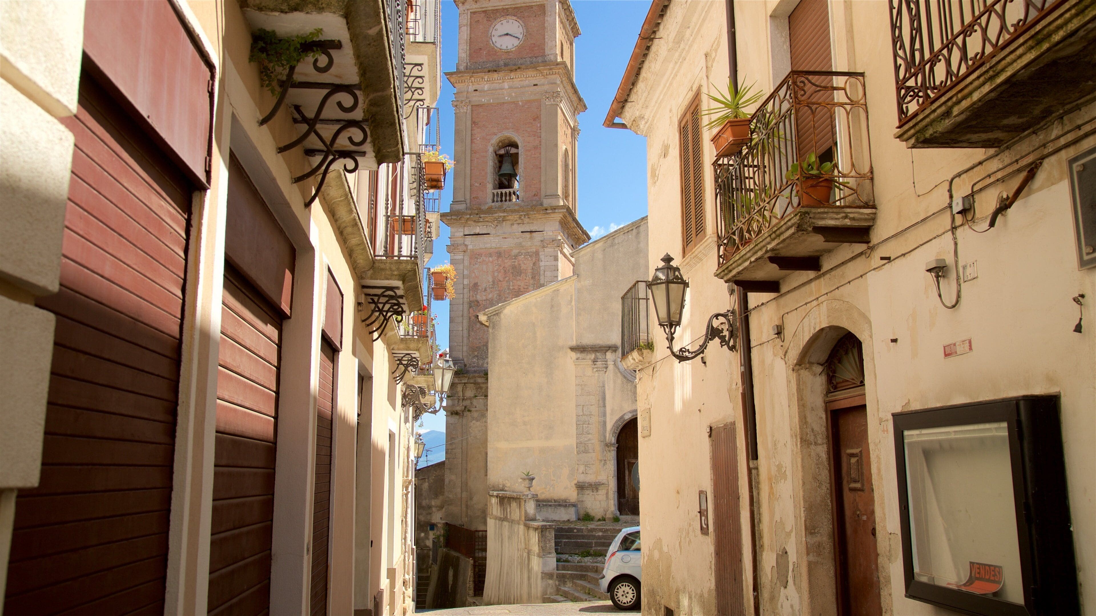 A narrow street with buildings, a clock tower, and a car.
