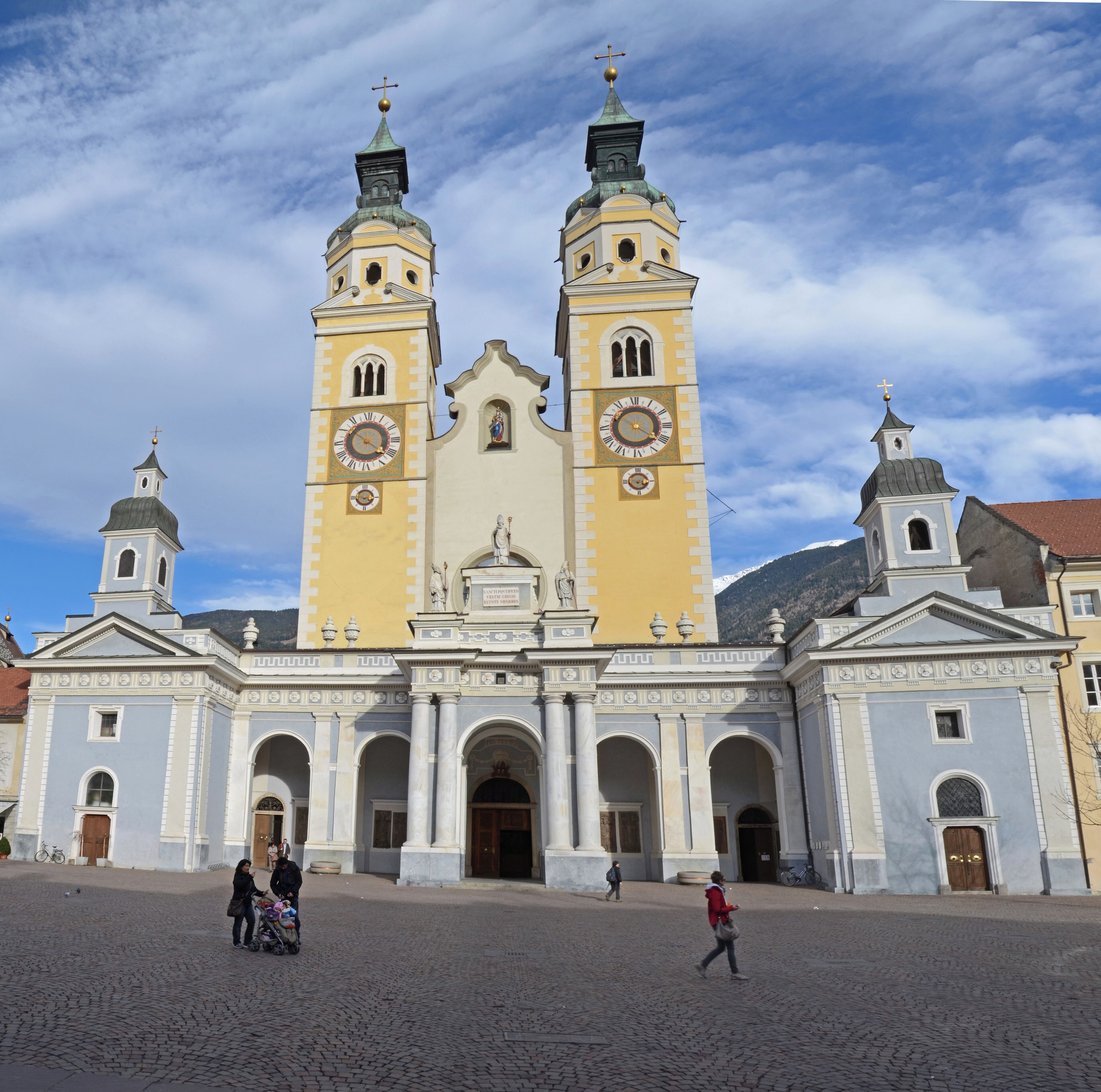 A historic church with two towers and a central dome, featuring a large clock and statues on the facade.