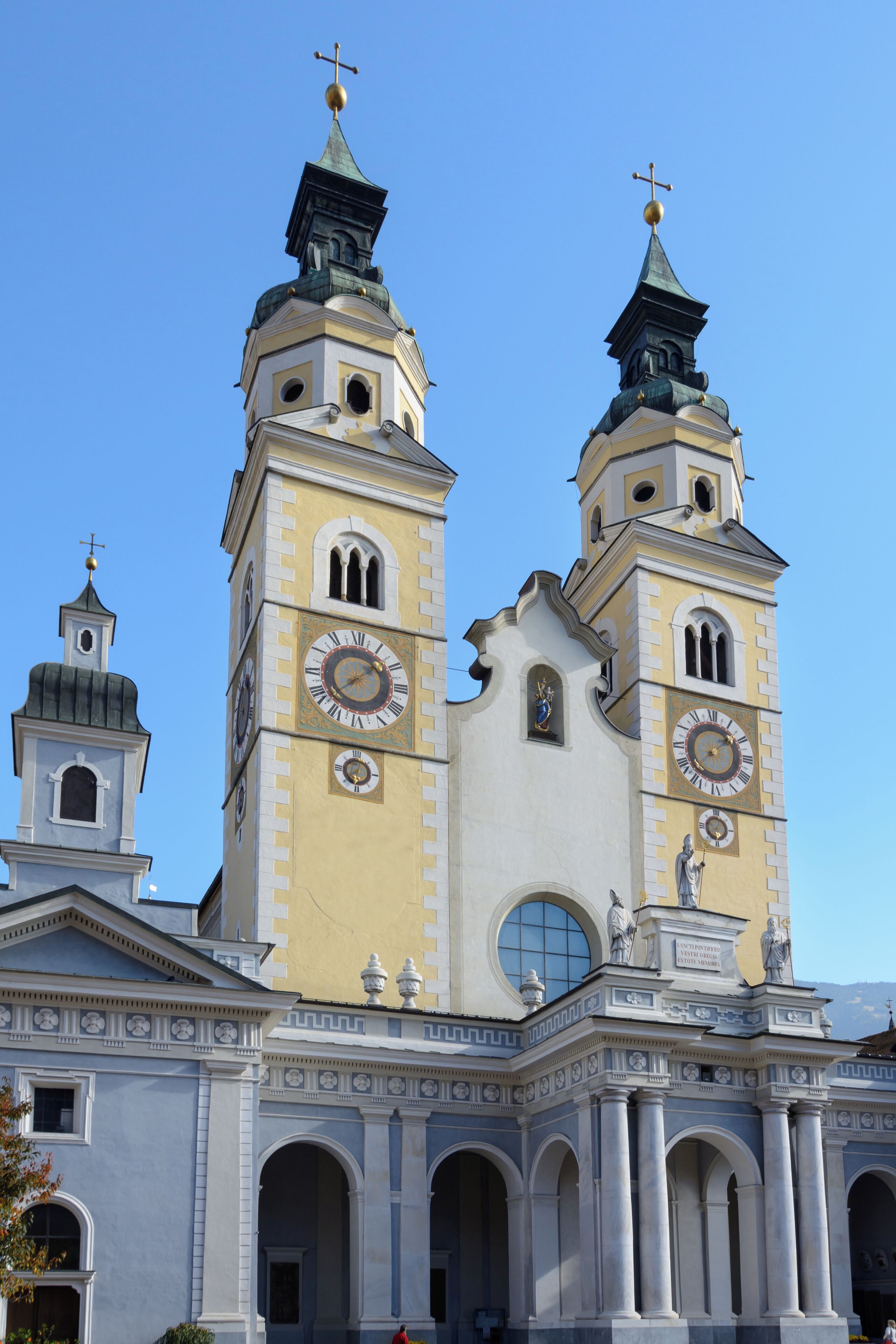 A large church with two towers, each featuring a clock and a statue on top.