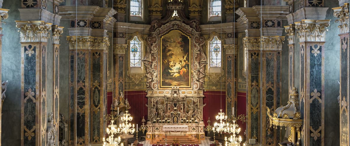 L’intérieur d’une église richement décorée, avec un autel principal imposant, des lustres et des œuvres d’art complexes ornant le plafond.