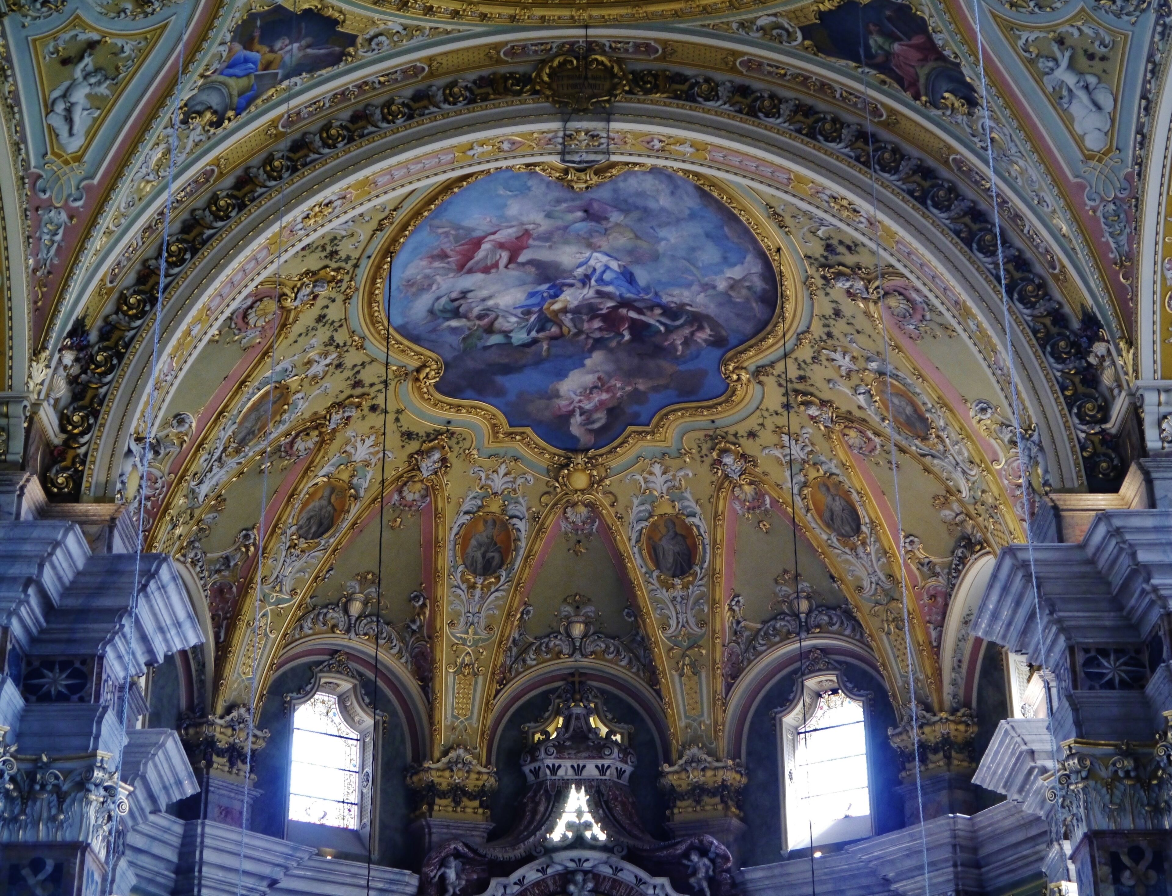 An ornate church interior with a large fresco, gold accents, and classical columns.