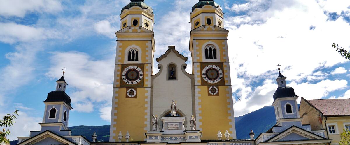 A church with two towers, a large clock, and statues in front.