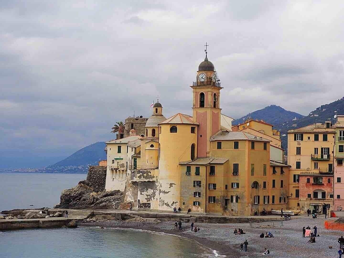 A coastal town with colorful buildings, a prominent church with a bell tower, and a rocky shoreline.