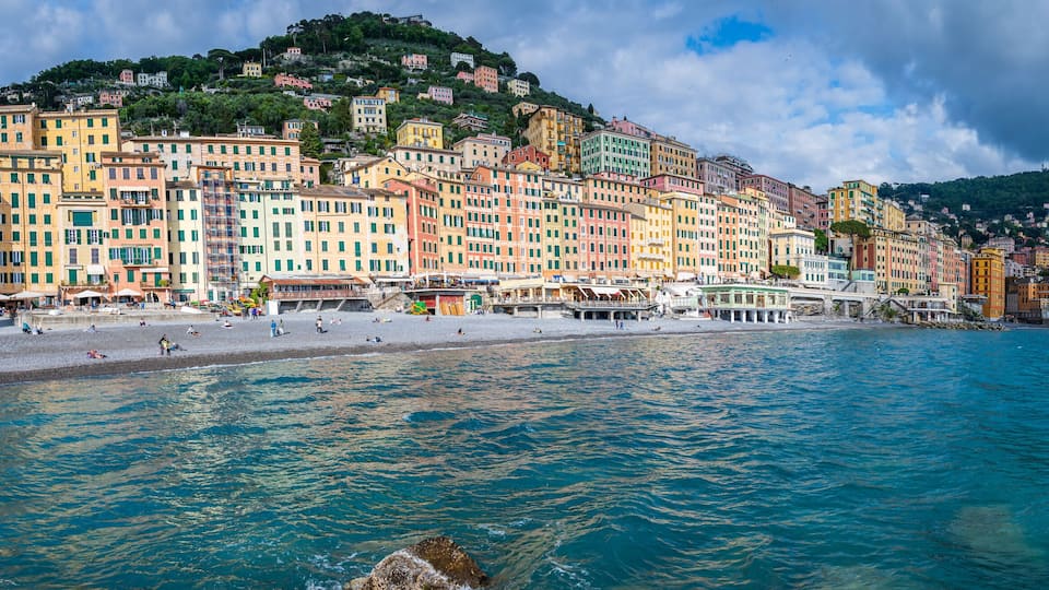 A coastal town with colorful buildings, a beach, and a mountainous backdrop.