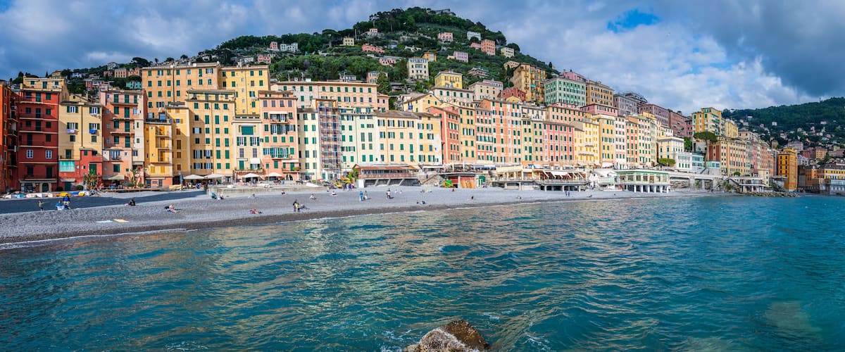 A coastal town with colorful buildings, a beach, and a mountainous backdrop.