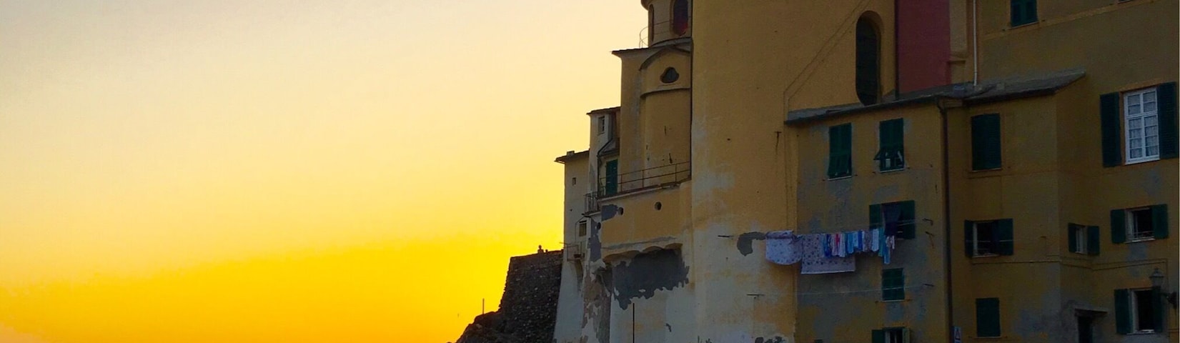 Una playa con gente al atardecer, una iglesia con campanario y edificios al fondo.