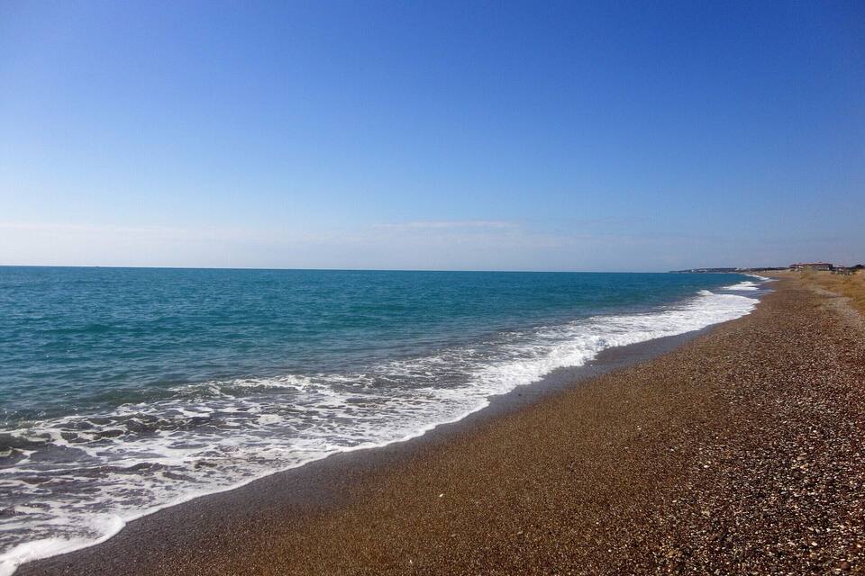 Een kiezelstrand met rustige golven onder een helderblauwe lucht.