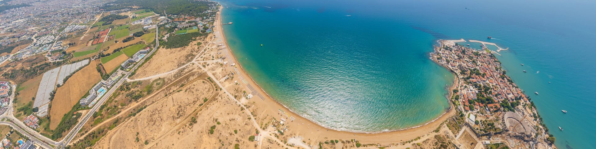 Side, Manavgat, Turkey. Wide aerial view of ancient peninsula and Buyuk Plaj (East Beach) with golden sand, turquoise water, archaeological ruins on summer day. Aerial view
