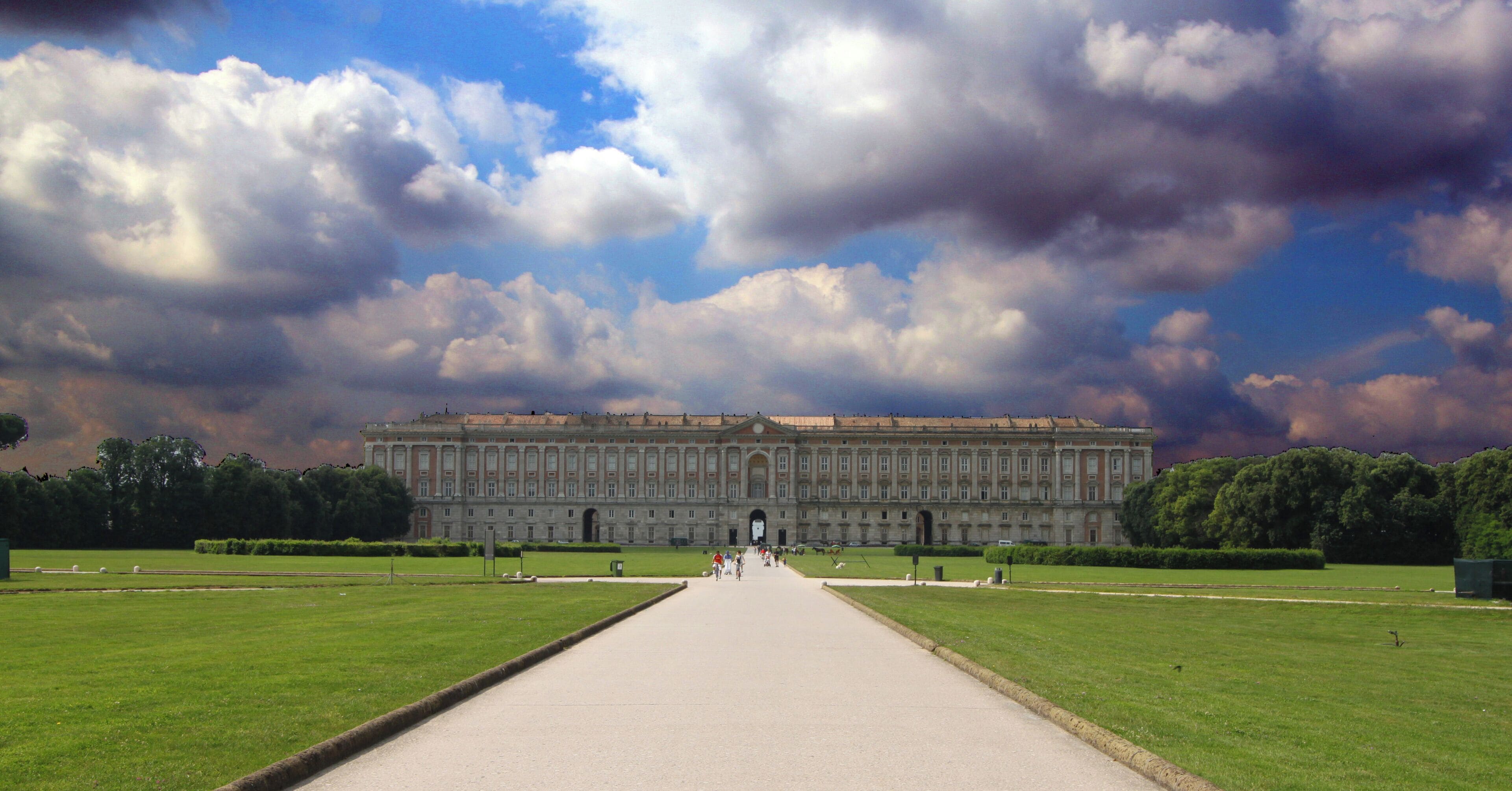 A grand building with a long central pathway leading to it, surrounded by green lawns and trees.