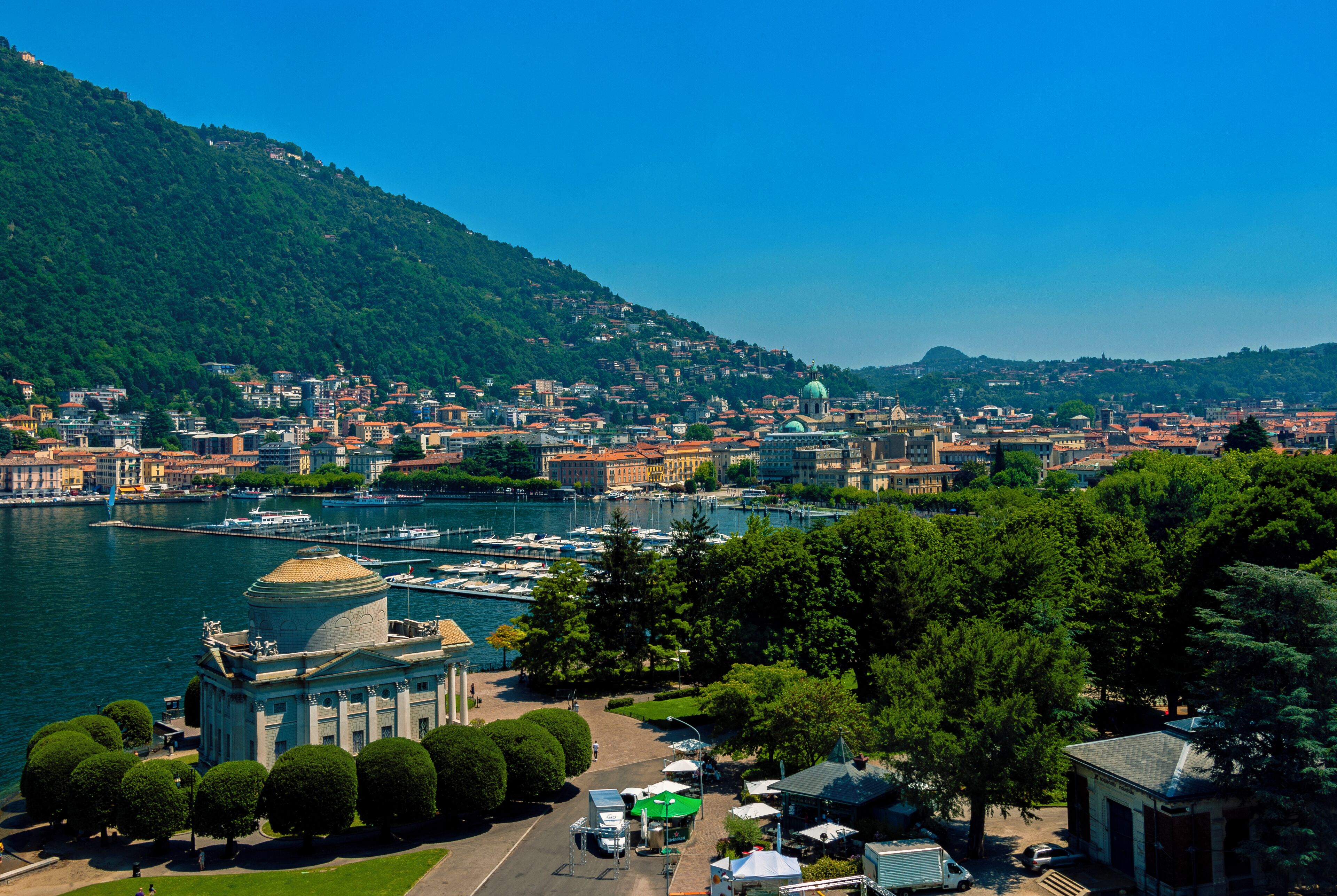A panoramic view of a city with a river, a prominent dome-shaped building, and a hill with dense greenery.