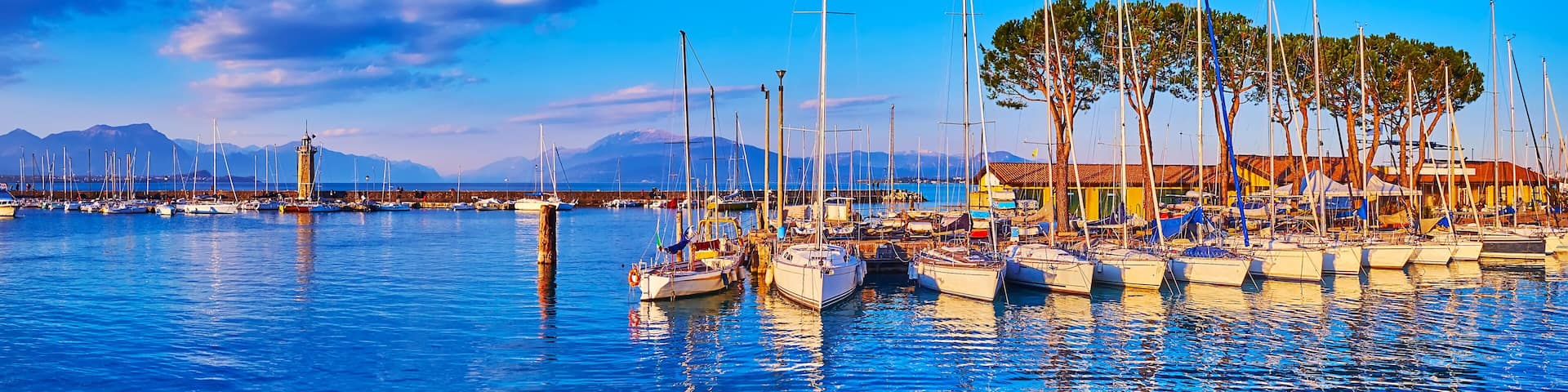 A marina with boats, a lighthouse, and mountains in the background.
