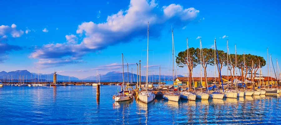 A marina with boats, a lighthouse, and mountains in the background.