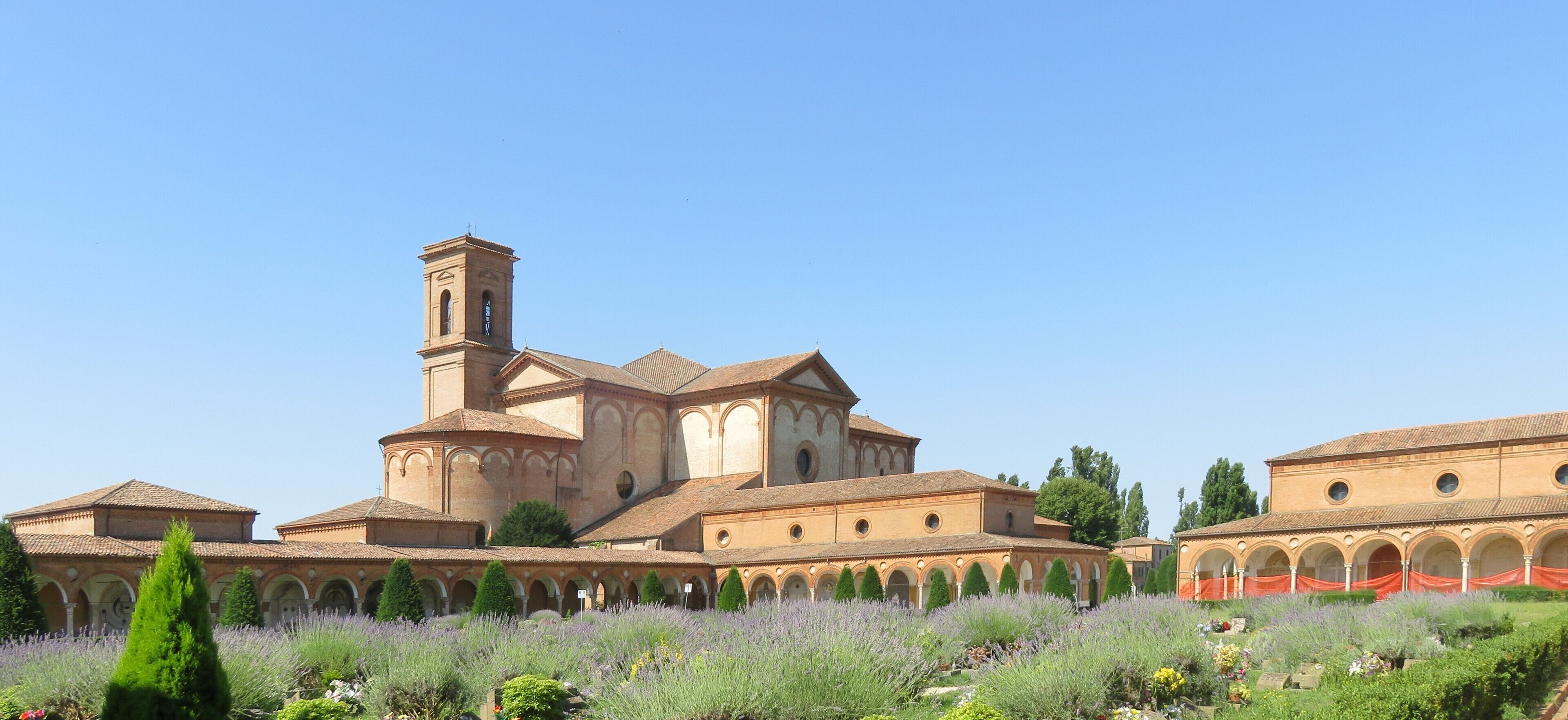 A historic monastery with a prominent bell tower, surrounded by a well-maintained garden with lavender and other plants.