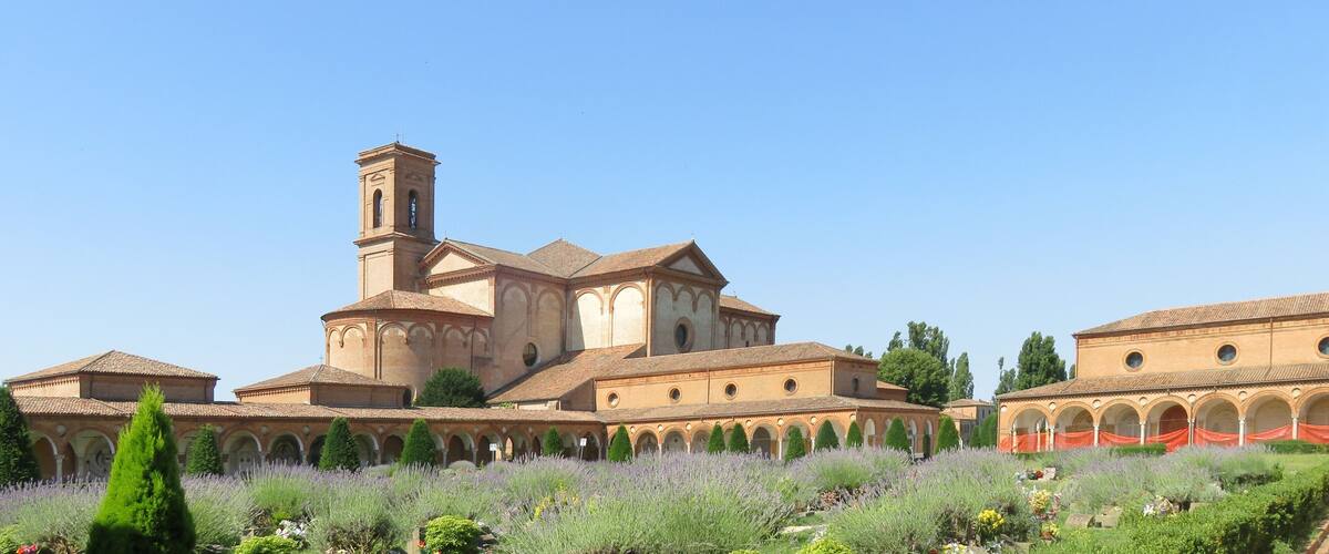 A historic monastery with a prominent bell tower, surrounded by a well-maintained garden with lavender and other plants.
